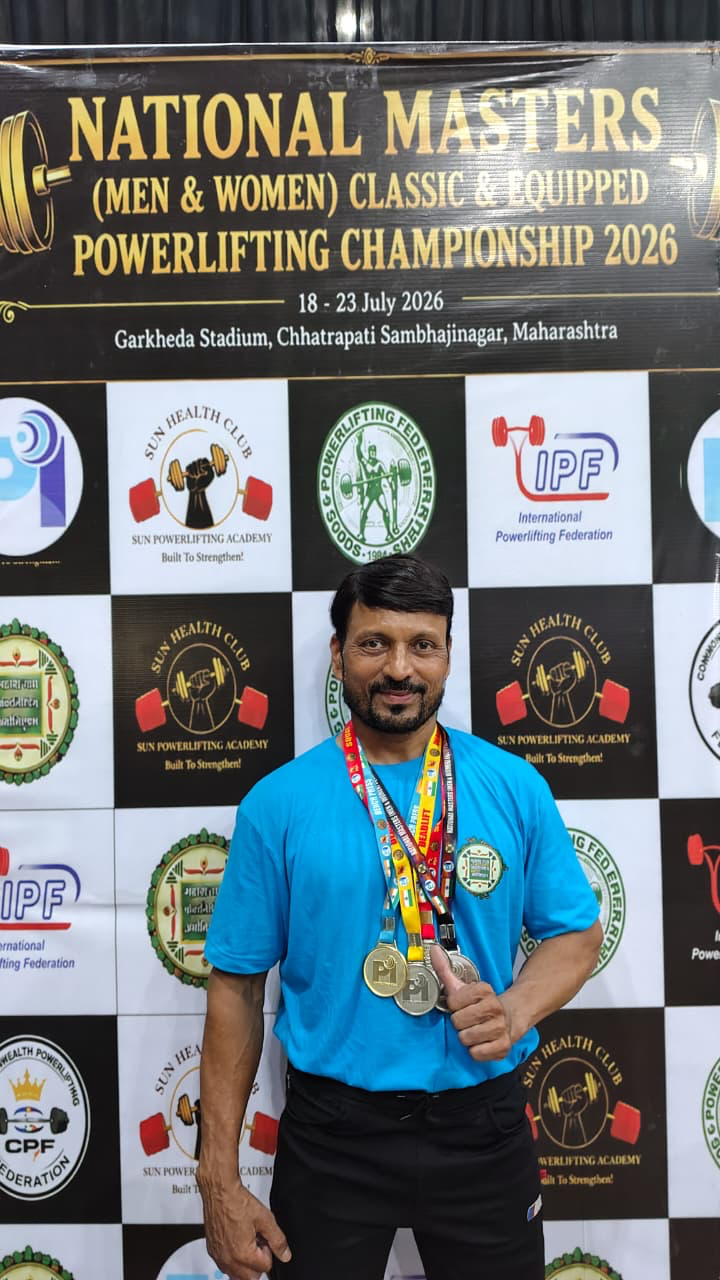 Coach Rajesh posing with medals in front of official IPF championship backdrop