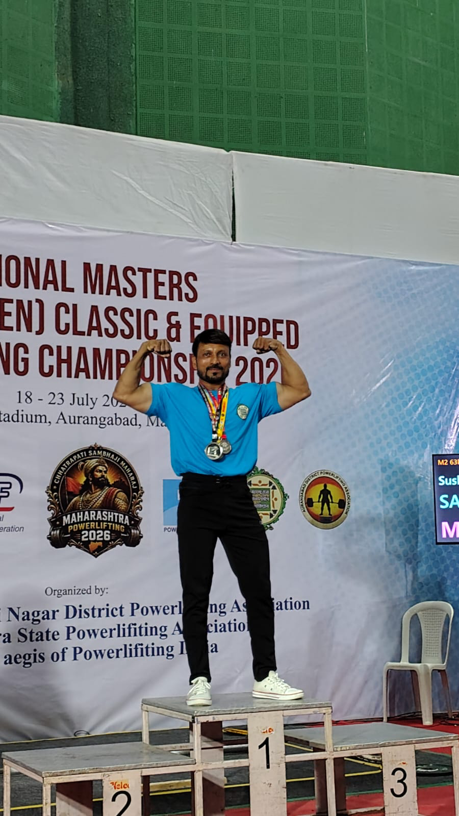 Coach Rajesh victory double bicep pose on 1st place podium with championship banner